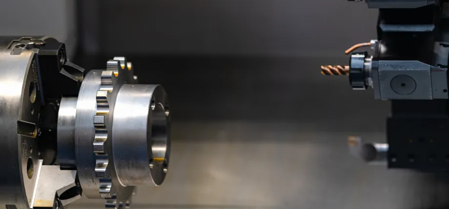 CNC lathe machining a carbon steel workpiece with visible gear features, using a drilling or boring tool for precision turning