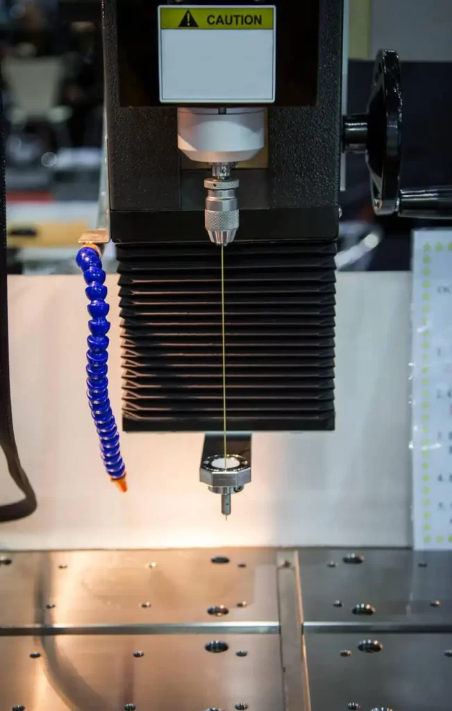 The image shows an industrial EDM hole drilling machine creating precision holes in a metal workpiece.