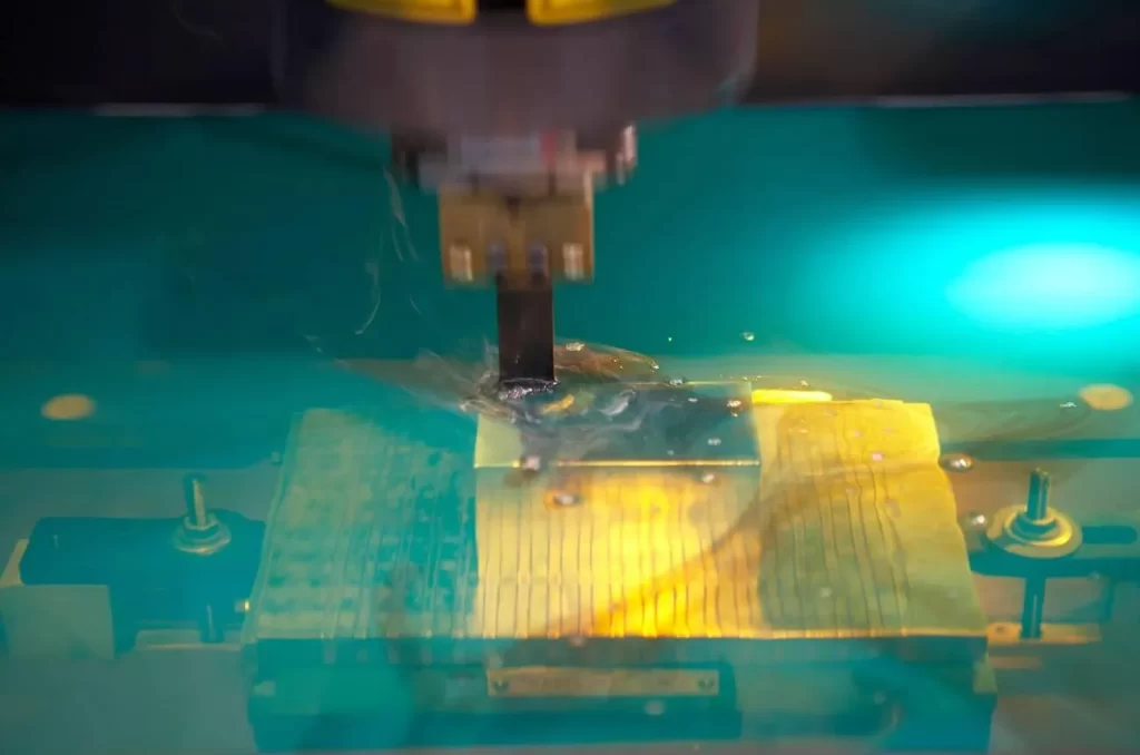 The image shows electrical-discharge machining, with the workpiece and electrode submerged in a dielectric liquid.