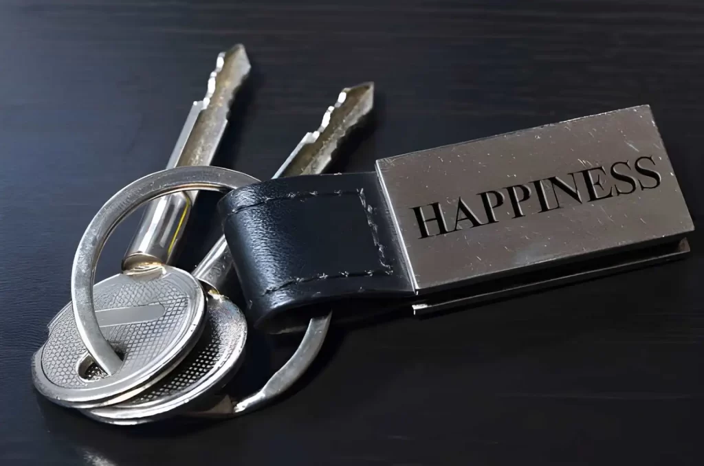 The image shows a stainless steel keychain with the word “Happiness” engraved on its surface.