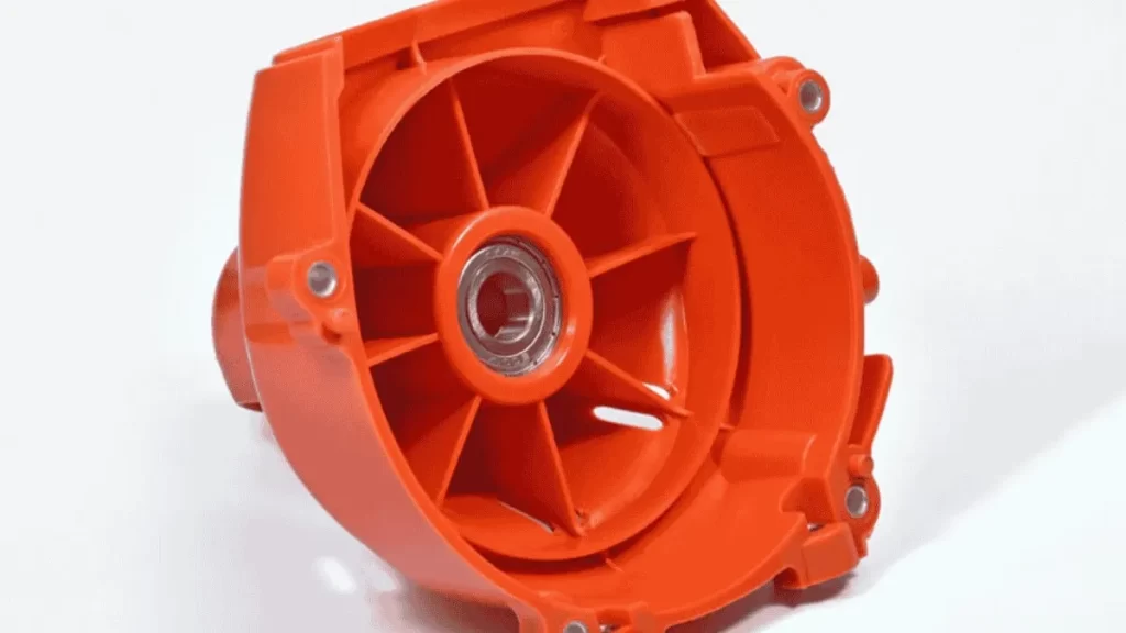 An orange insert molded part displayed on a white background. A metal component is embedded at the center, showing the combination of plastic and metal in one molded piece.