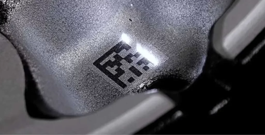 The image shows a metal surface with a laser-etched QR code.