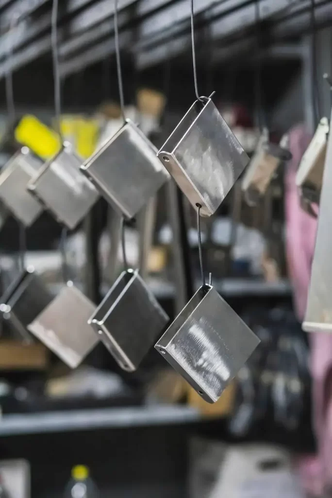 The image shows metal parts hanging and awaiting the painting process in a factory setting.
