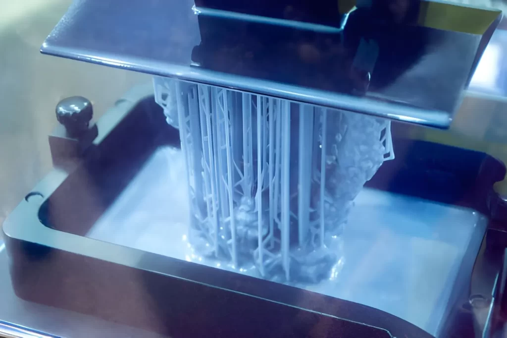 The image shows the working of a stereolithography (SLA) 3D printer, where the build platform is lowered into a liquid photopolymer resin.