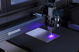 A laser engraving machine is working on a metal sheet with purple light