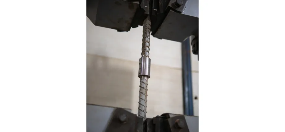 Threaded carbon steel specimen gripped in a universal testing machine during tensile strength testing for material properties evaluation.