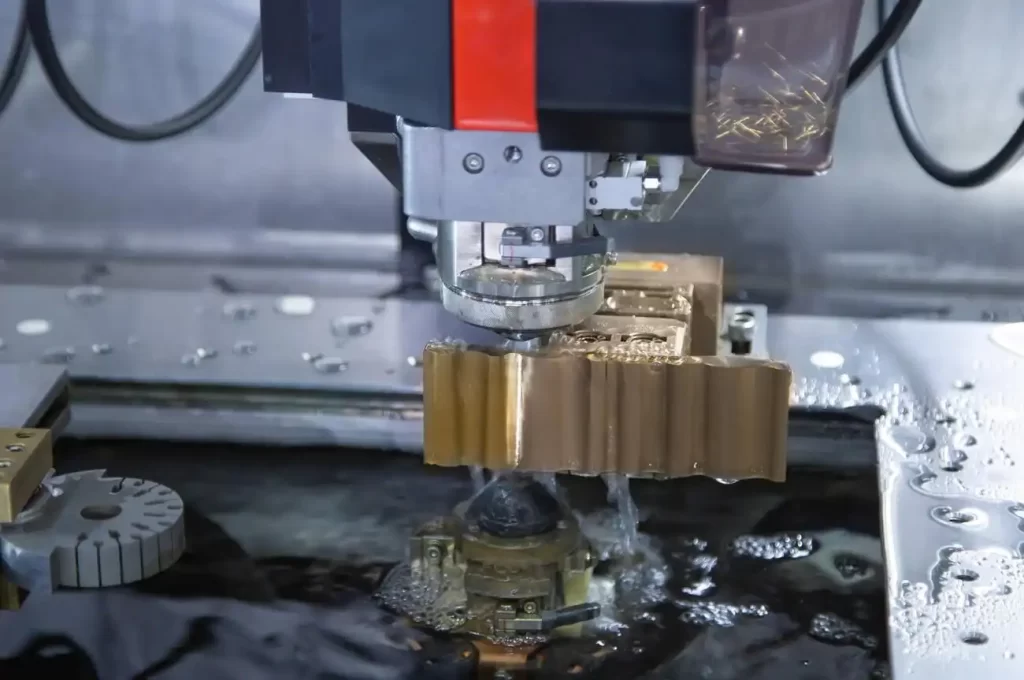 The image shows an automatic wire threader machine cutting a small hole in a brass workpiece during wire EDM machining.