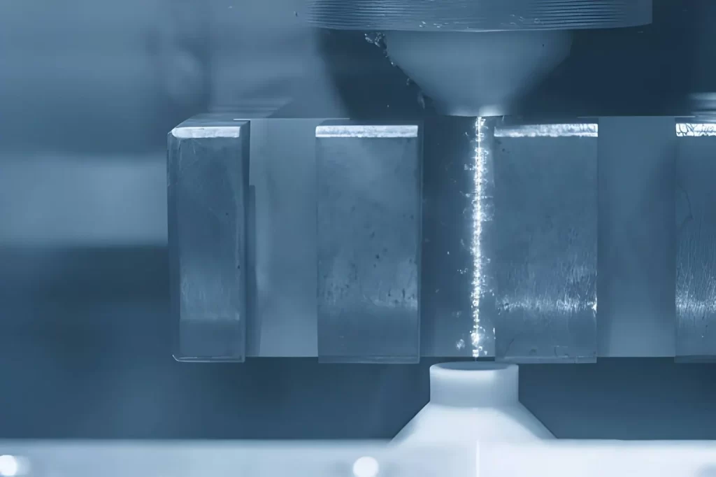 The image shows a close-up of a CNC-controlled wire EDM machine during machining, with a blue-toned appearance.