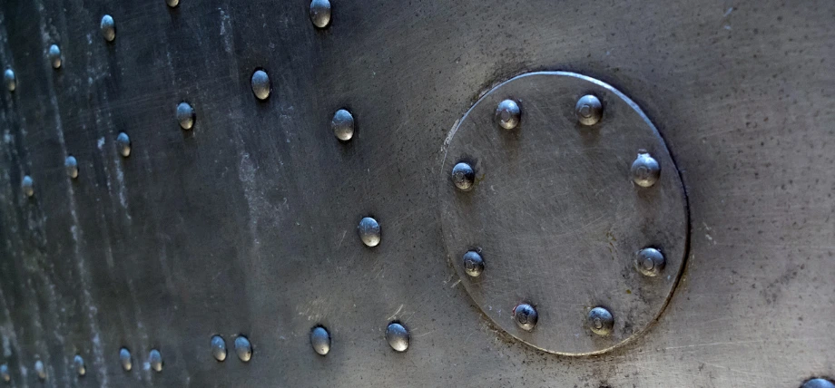 Close-up of aircraft-grade solid rivets installed flush with surrounding metal skin, showing uniform round heads and permanent fastening.