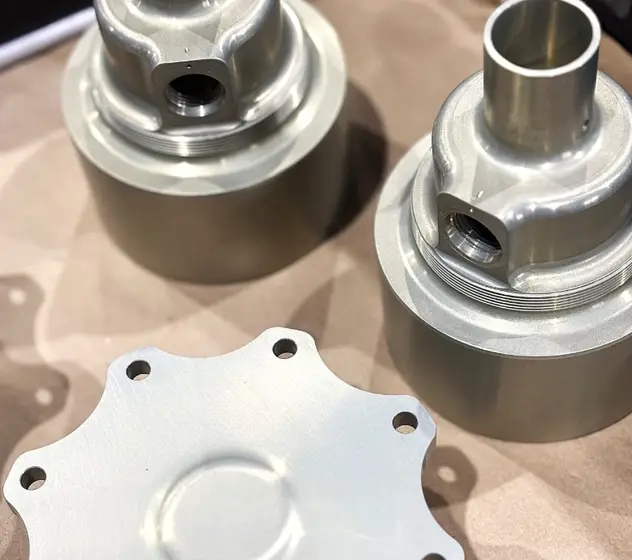 Three chromic acid anodized aluminum aerospace components — two threaded cylindrical housings and a bolt-pattern flange plate.