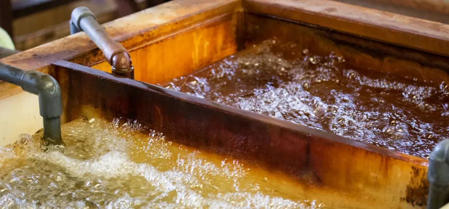 A multi-compartment industrial immersion tank containing bubbling, amber-colored electrolyte liquid with integrated inlet and outlet piping.