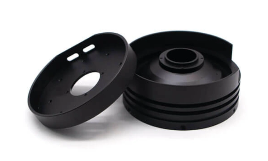 Two black-anodized aluminum machined components with ribbed housing and circular lid on a white background