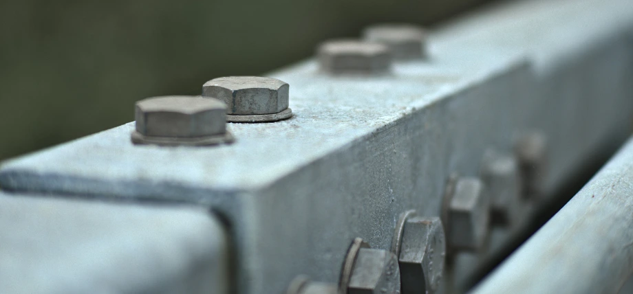 Row of rusted hex bolts securing heavy steel beams outdoors, illustrating rivets vs bolts in structural applications.