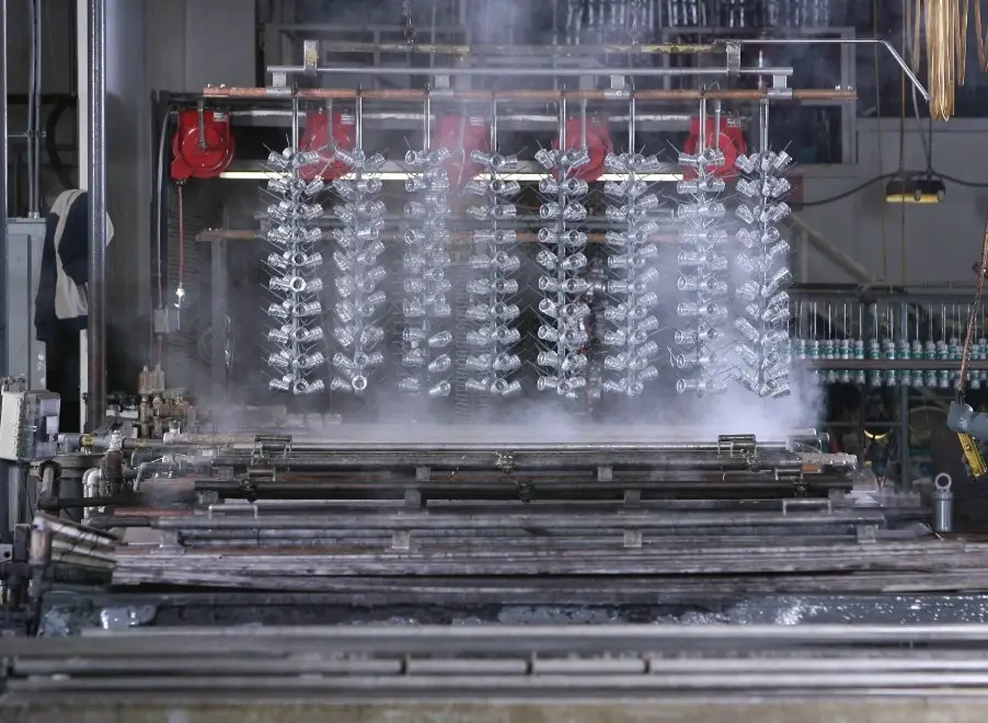 Aluminum parts racked on anodizing jig being lifted from steaming chromic acid bath in industrial facility