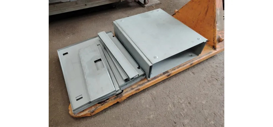 Stack of powder-coated sheet metal panels and folded sections laid flat on a yellow pallet truck, prepared for electrical enclosure assembly.