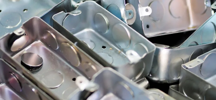 Stack of finished galvanized sheet metal electrical junction boxes with knockouts and mounting ears, ready for installation during sheet metal box fabrication.