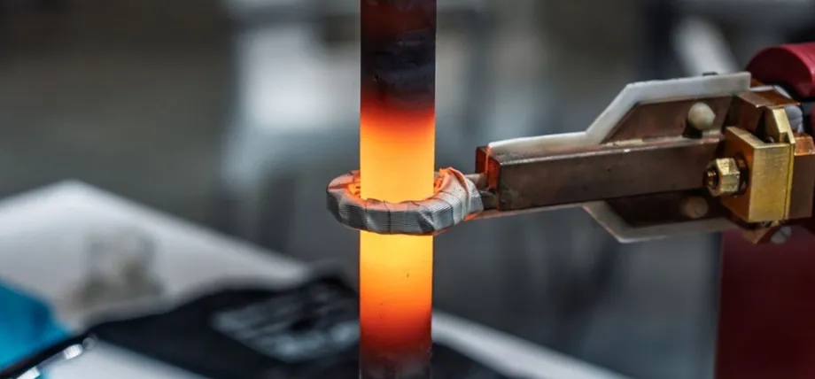 A cylindrical 4140 alloy steel bar being rapidly heated by an induction coil, glowing bright orange-red at the contact zone with intense thermal gradients visible.