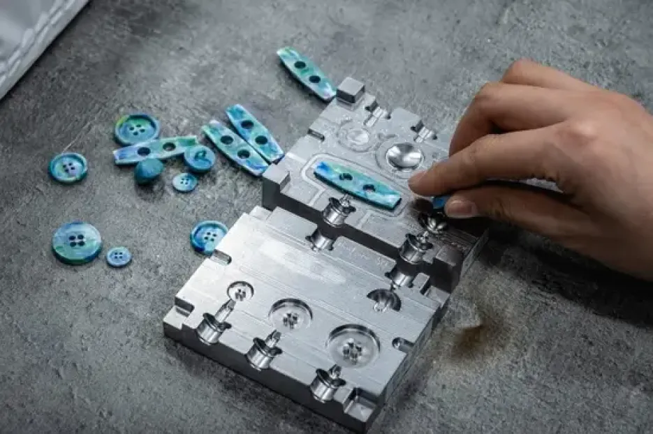 Hand extracting tiny blue molded plastic parts from an open metal micro mold