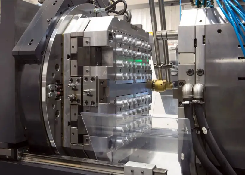 Close-up of an industrial injection molding machine with an open steel mold and freshly ejected transparent plastic parts.