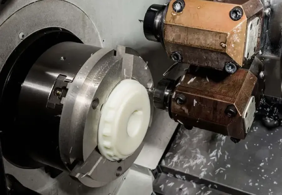 CNC lathe turning a white plastic part with a cutting tool and chips