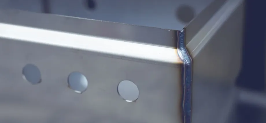 Close-up of a precise TIG-welded corner seam with rainbow heat tint on a stainless steel enclosure during sheet metal box fabrication.