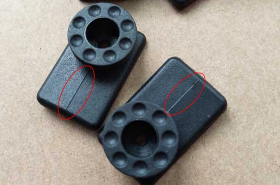 Two black injection-molded plastic parts with weld lines highlighted by red circles on each part's surface