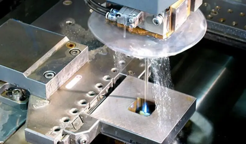 Wire EDM machine cutting through a metal mold block with water coolant flow