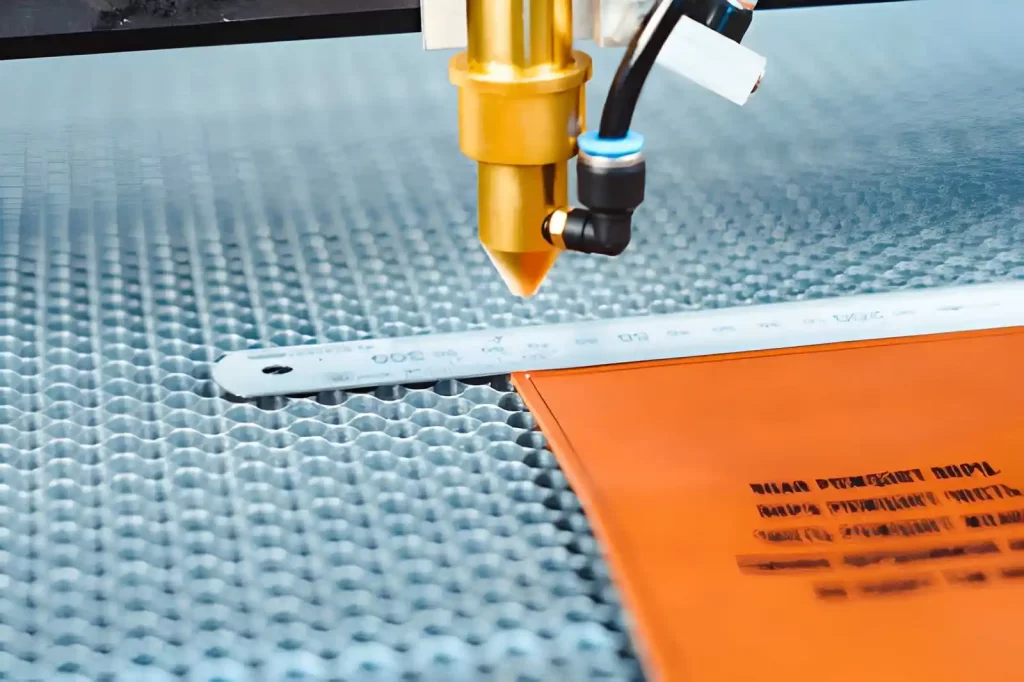 The image shows a CO₂ laser cutting machine cutting the corners of a plastic sheet, with a scale placed for reference.
