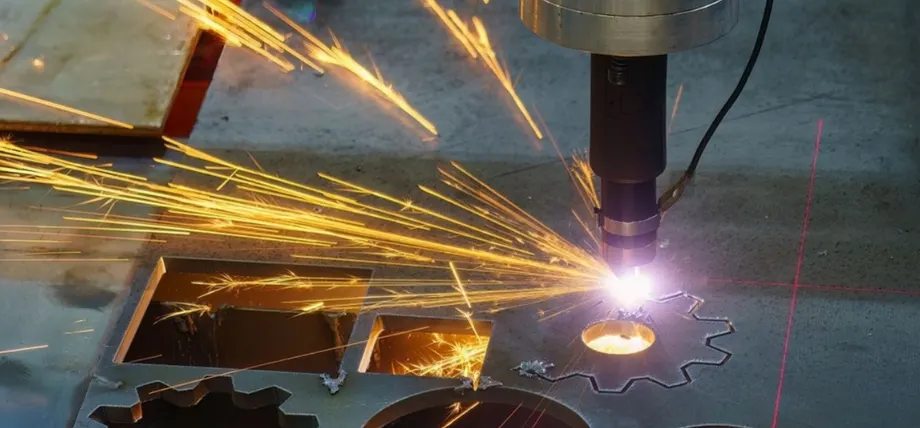 Automated fiber laser head cutting complex designs into a metal plate on a support grid, emitting bright light.