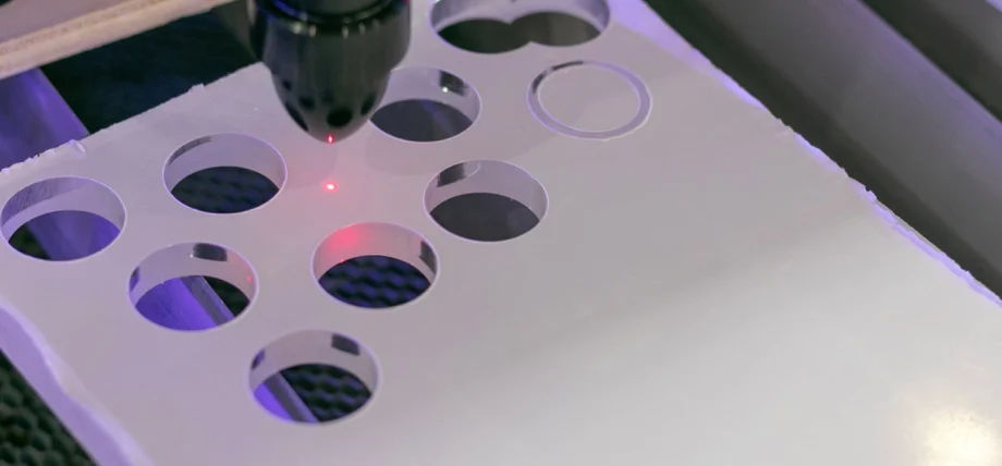 Laser beam actively cutting circular holes in a white material, perforations visible under focused red light.