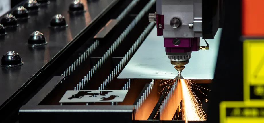 Laser beam melting and cutting through a metal plate, with glowing molten edge and ejected sparks.