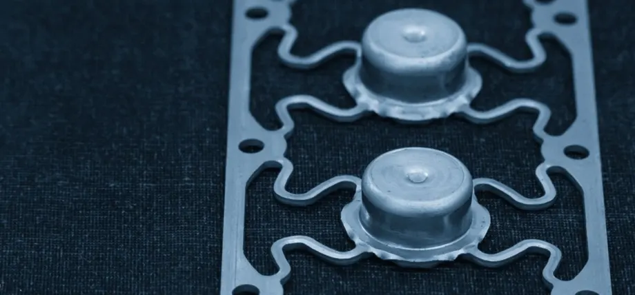 Laser-cut metal component with two cylindrical protrusions and intricate wavy cutouts.