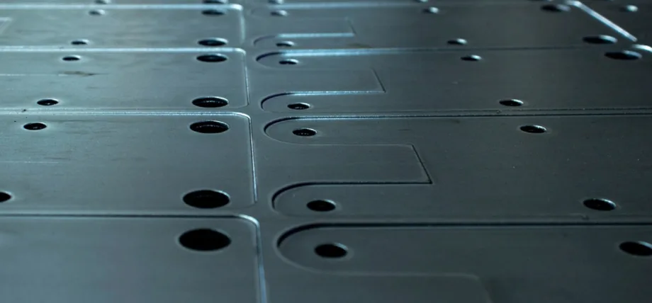 Array of metallic plates with laser-etched holes, slots, and markings.