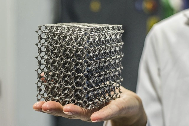 A person holding a metal 3D printed lattice cube structure