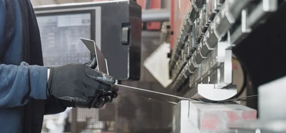 Worker carefully positioning a metal sheet into a press brake machine for bending in a contract manufacturing setting.