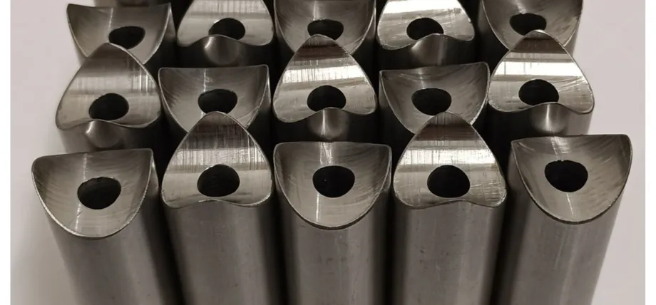 A collection of identical machined metal pipes showing smooth, reflective contoured end faces and center bore holes
