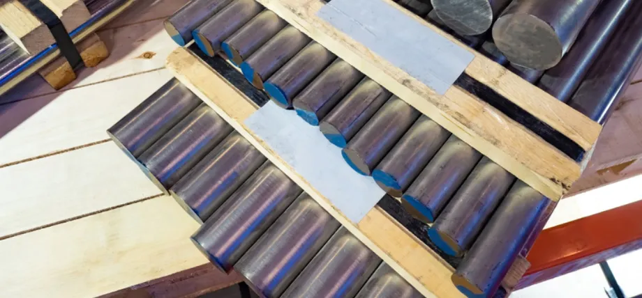 A stack of cylindrical aluminum billets with blue-painted ends organized in a wooden crate for transport.