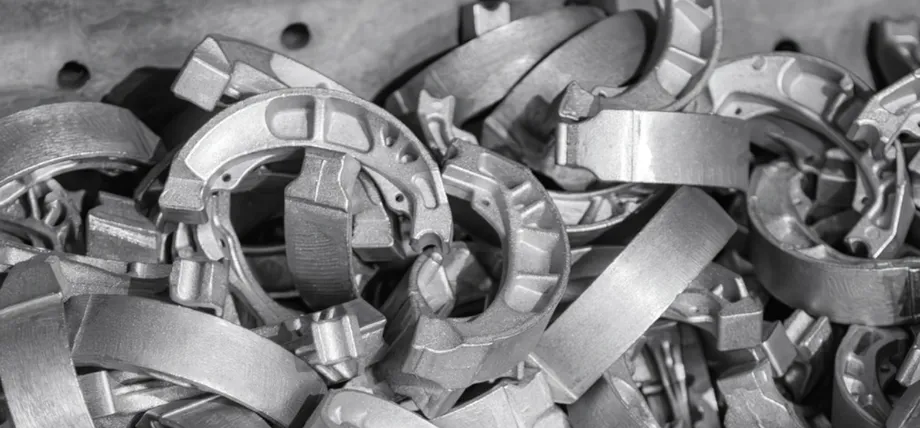 A large collection of raw cast aluminum brake shoe components is piled together in a storage bin.