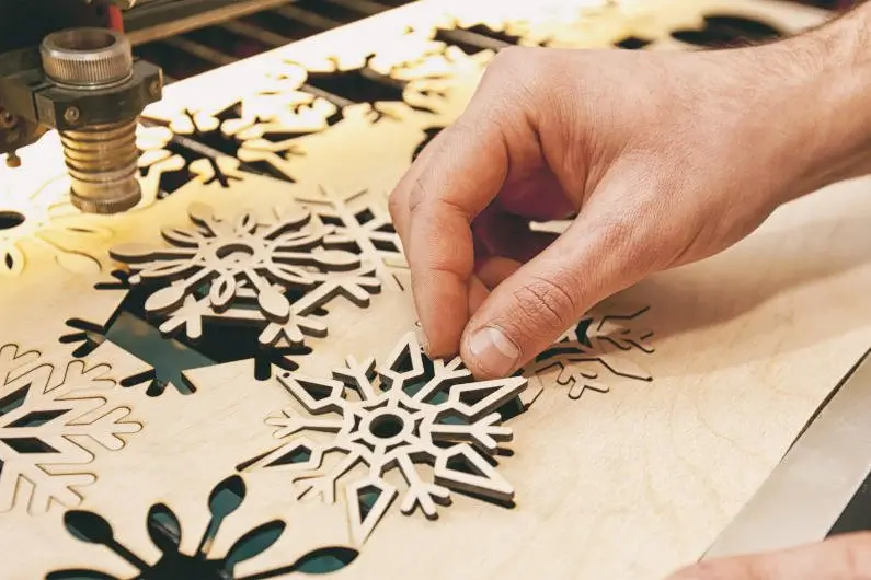Hand removing snowflake design cut by CNC laser on wood