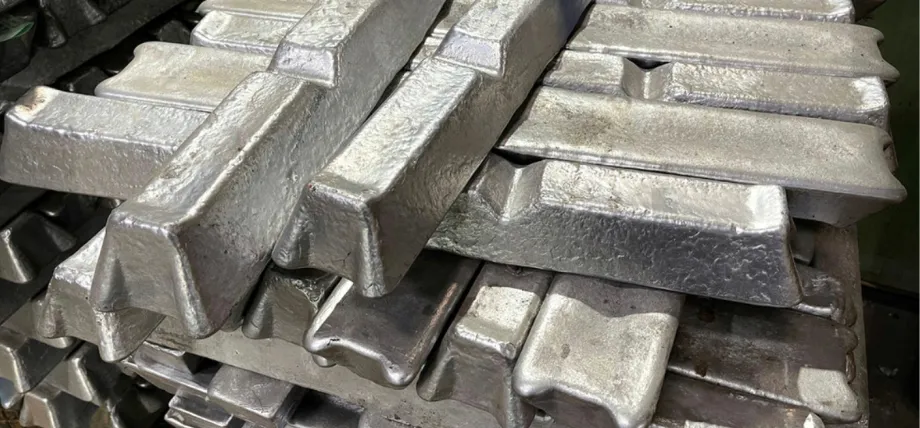 A stack of rough-textured, cast aluminum ingots with a metallic sheen, piled haphazardly in a storage area.