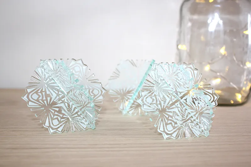 Three decorative pieces of glass cut by laser are placed on a table top with a blur jar in the background