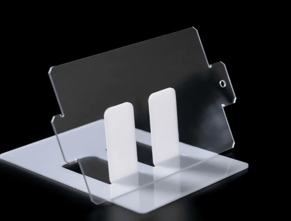 A thin polycarbonate piece cut by laser, placed diagonally against a white support with a black background