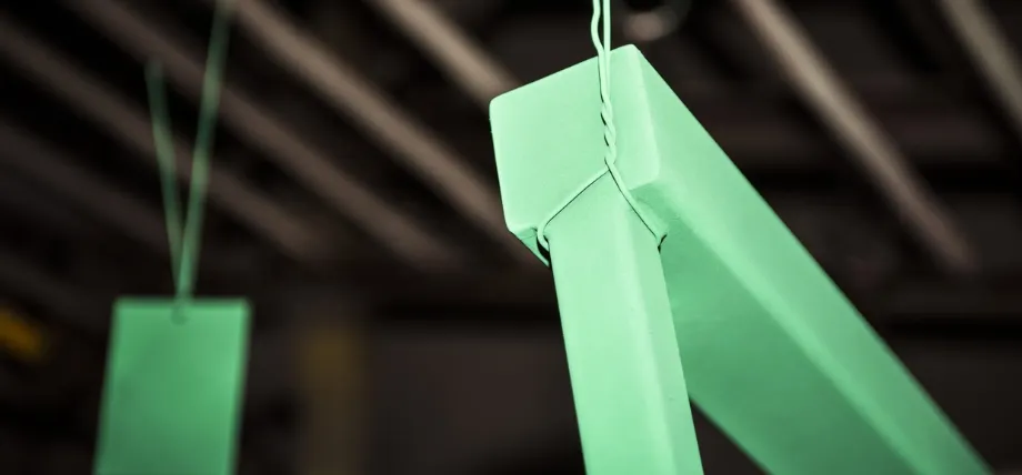 Rectangular metal parts hanging from wires in a factory setting, freshly coated in a vibrant, matte mint green powder finish.