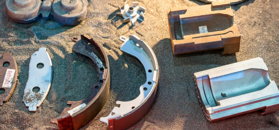 Various metal parts and mold halves are placed on a bed of casting sand, demonstrating the sand casting technique.