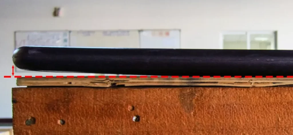 Warped black injection-molded plastic part elevated above a flat surface, with a red dashed reference line highlighting the deformation gap