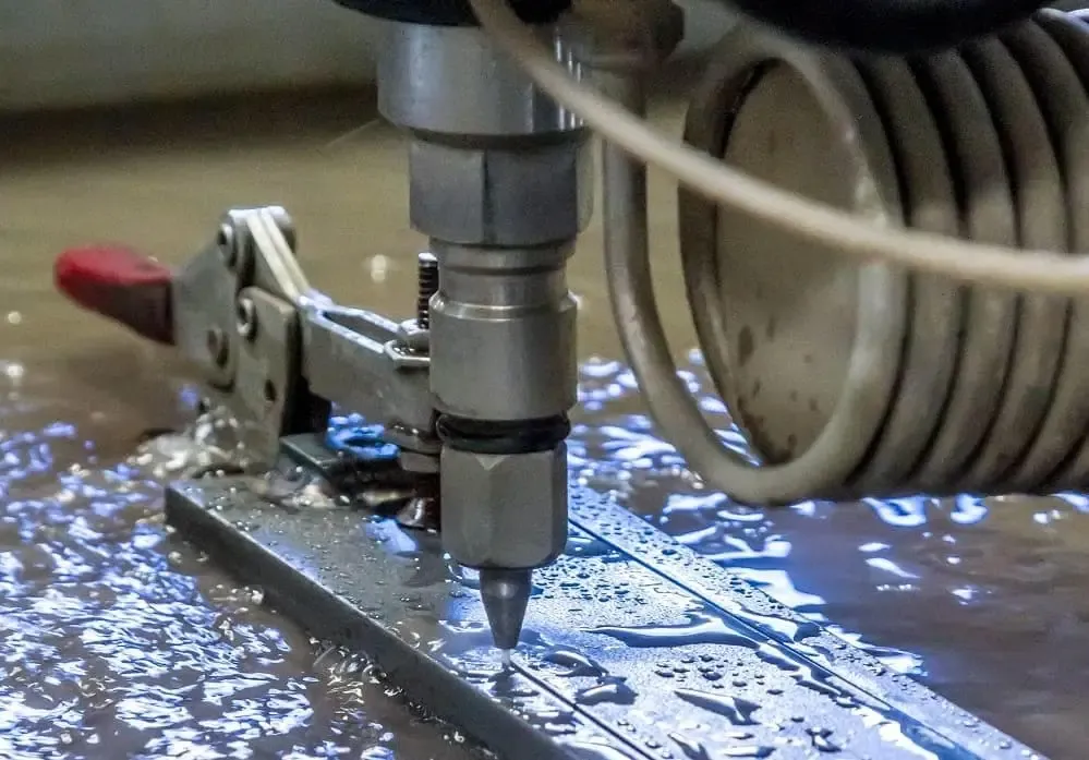 waterjet cutting machine creating a cut on a sheet metal prototype with water spray visible in the surroundings.