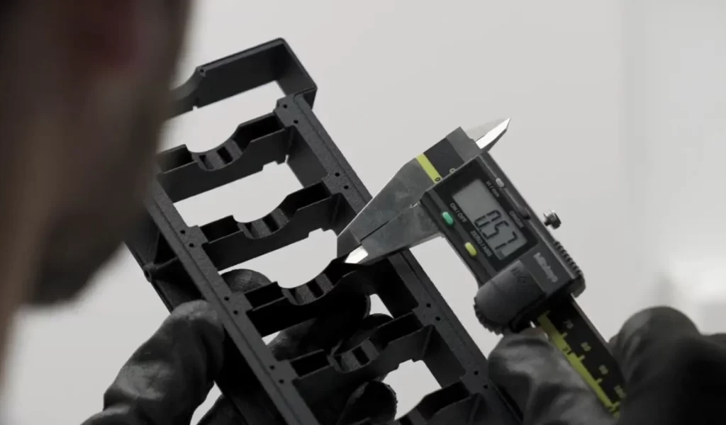 Digital caliper measuring tolerance on black 3D printed part in gloved hands