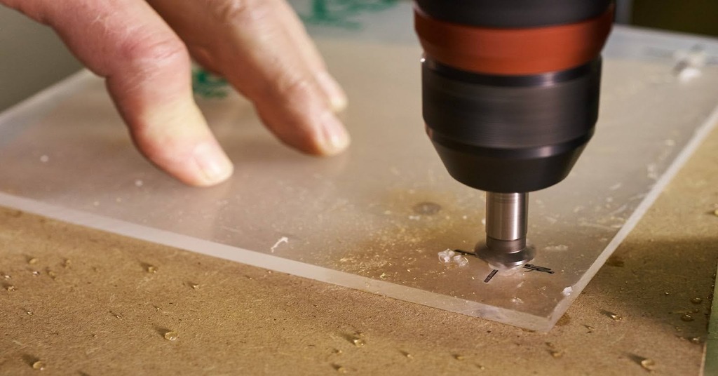 The image shows a CNC drilling machine creating holes in a transparent acrylic sheet