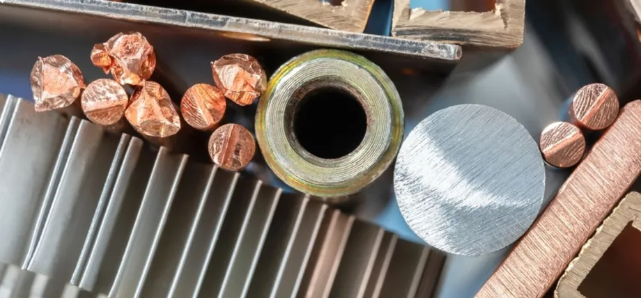 A top-down view of various non-ferrous metal samples, including copper rods, aluminum fins, and brass extrusions.