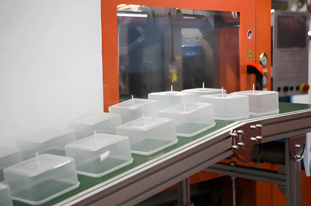 Multiple identical transparent square plastic enclosures on a conveyor.